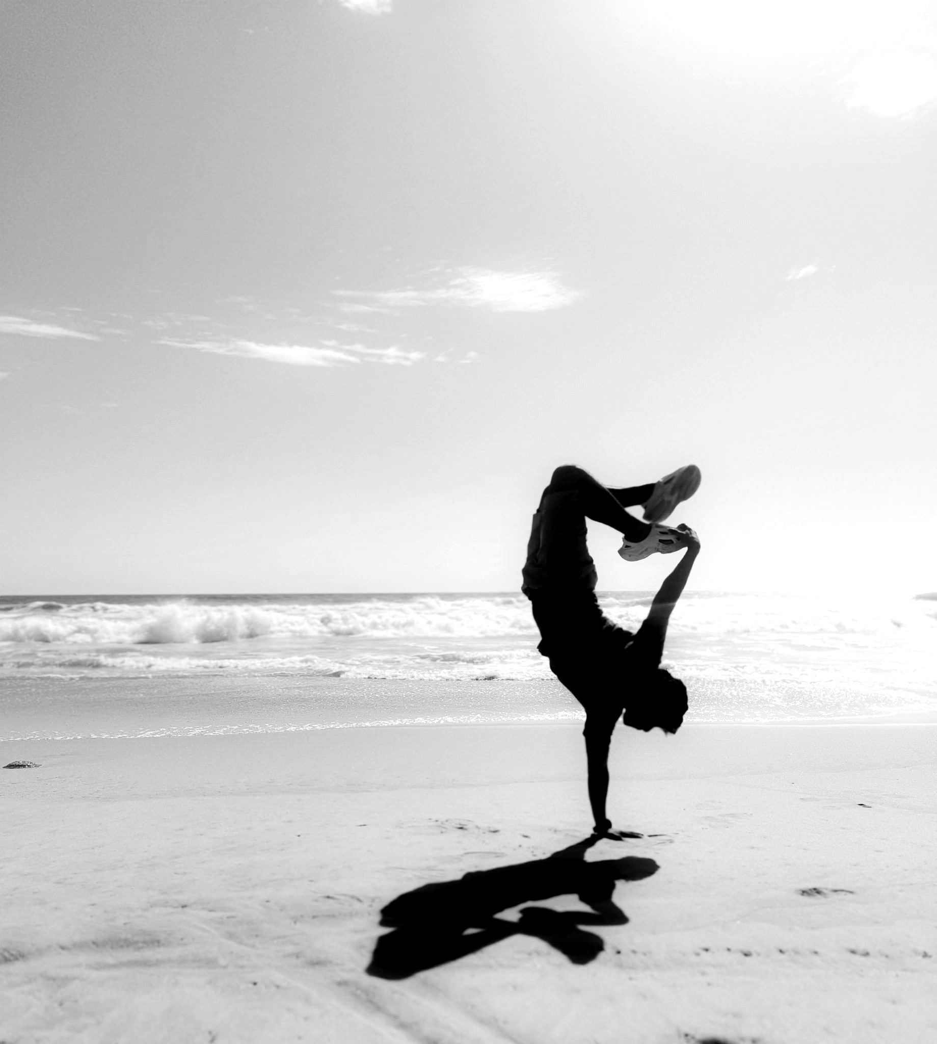 Silhouette of an athlete holding a one-arm handstand at the water’s edge